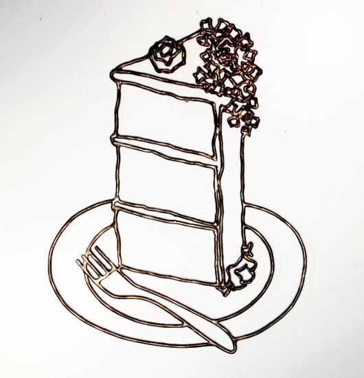 Modern, contemporary art: a wall-hanging polished metal sculpture in cast bronze filigree, the design features the abstract geometric lines and organic swirls of a decadent three-tired cake with rose petal frosting; inspired by the infamous quote by Marie Antoinette, "Let them eat cake!" and is displayed on a white background.