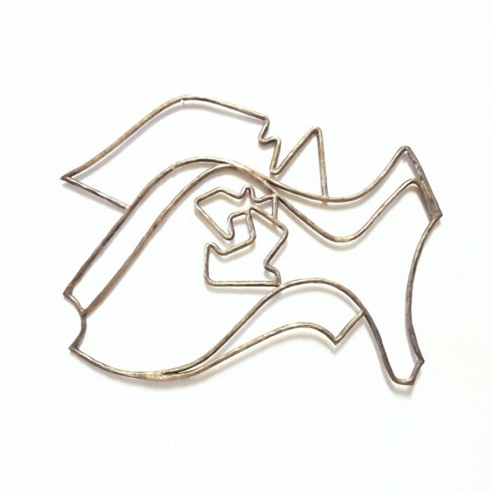 Modern, contemporary art: a wall-hanging metal sculpture in cast bronze filigree, the design features the polished geometric lines and organic swirls of an abstract punk rock fish with anarchy arrows and a mohawk displayed on a white background.
